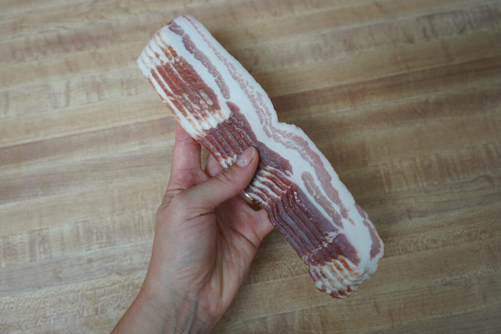 a hand holding slices of bacon