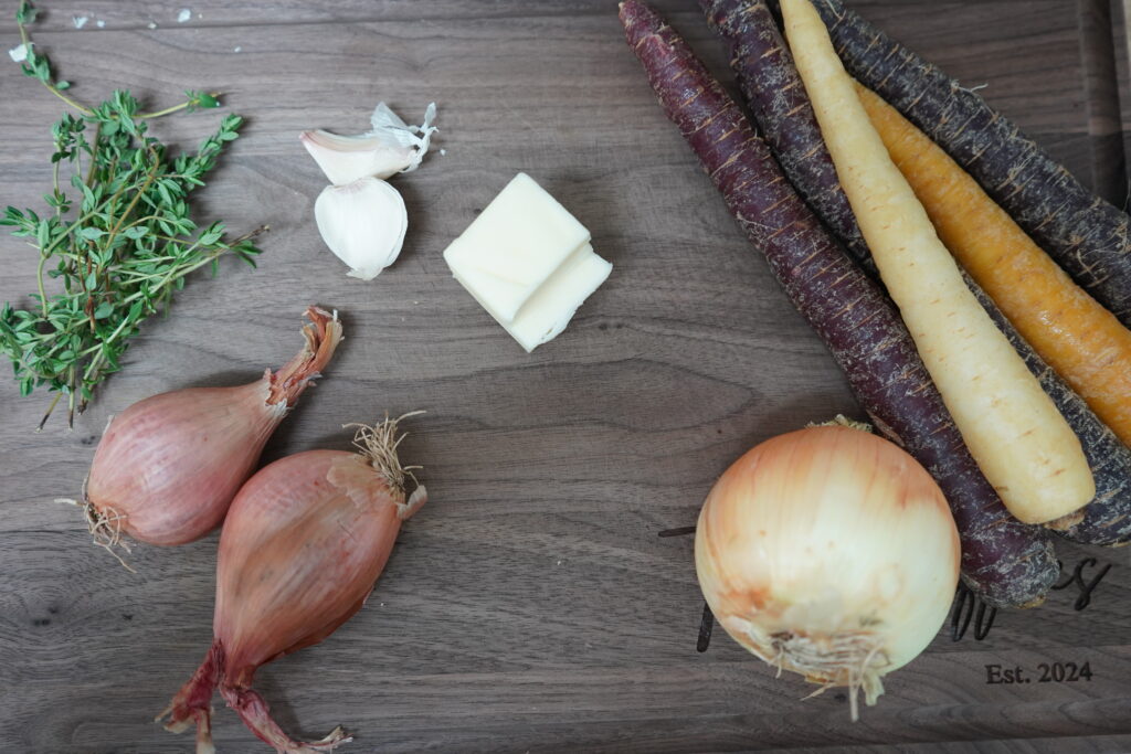 onion, carrots, garlic, thyme and butter on a cutting board