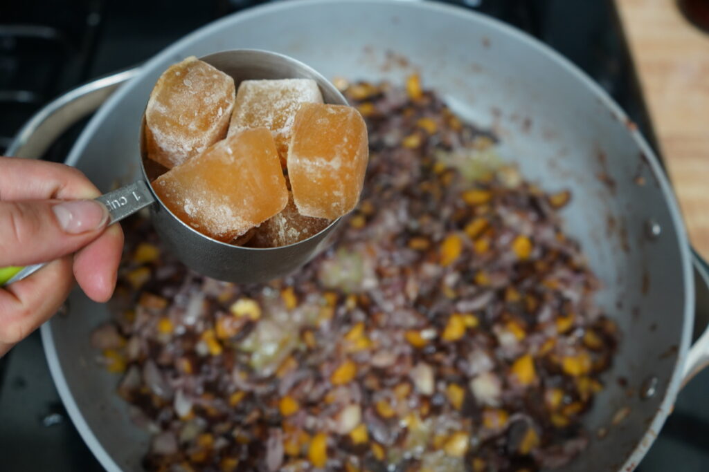 frozen cubes of broth being added to a pan of vegetables