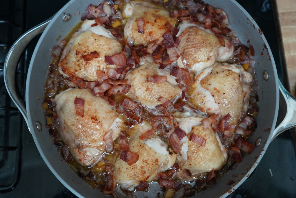 chicken thighs in a pan topped with chopped bacon