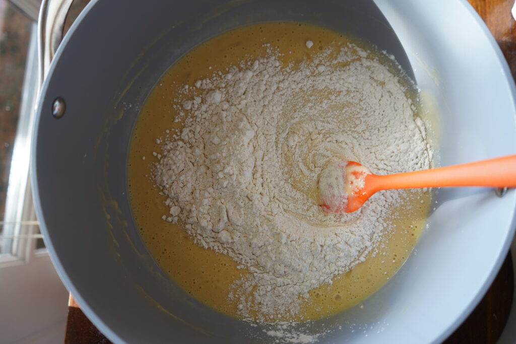 fresh flour poured over watery dough being mixed with a spatula