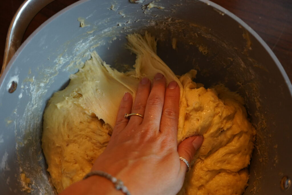 a hand pulling the dough away from the sides of the mixing bowl