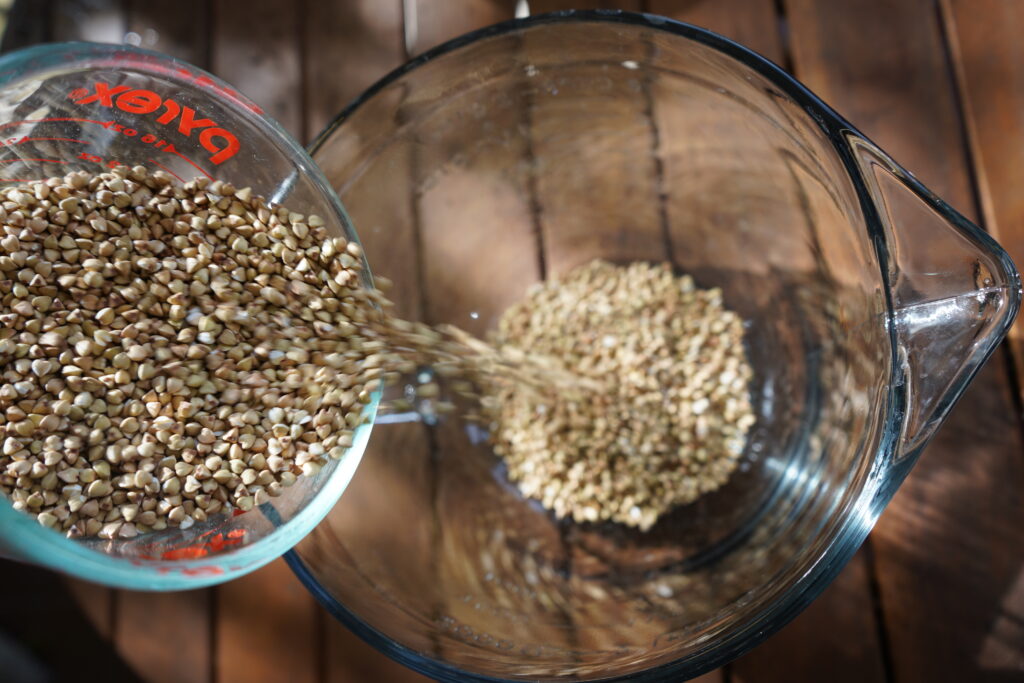 a measuring cup pouring buckwheat into a glass mixing bowl