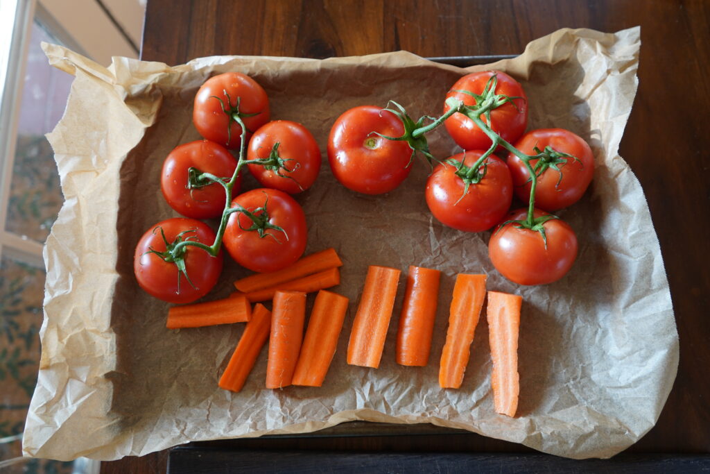 a parchment lined baking sheet with tomatoes and carrots on it