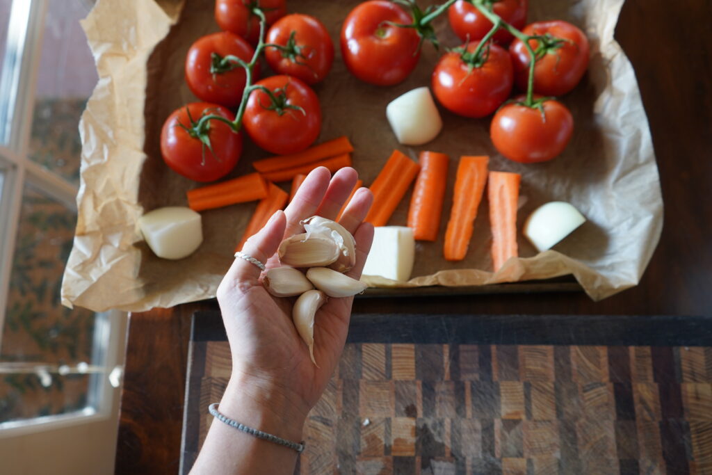 a hand holding garlic cloves over a baking sheet with vegetables on it