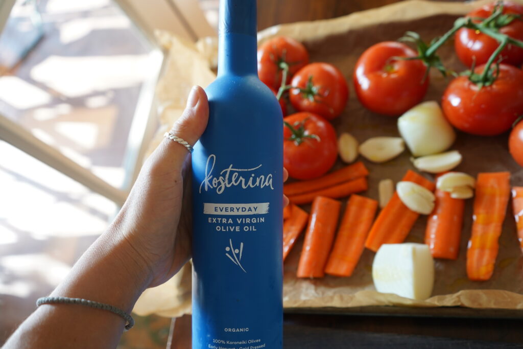 an olive oil bottle about to be poured on a pan of vegetables