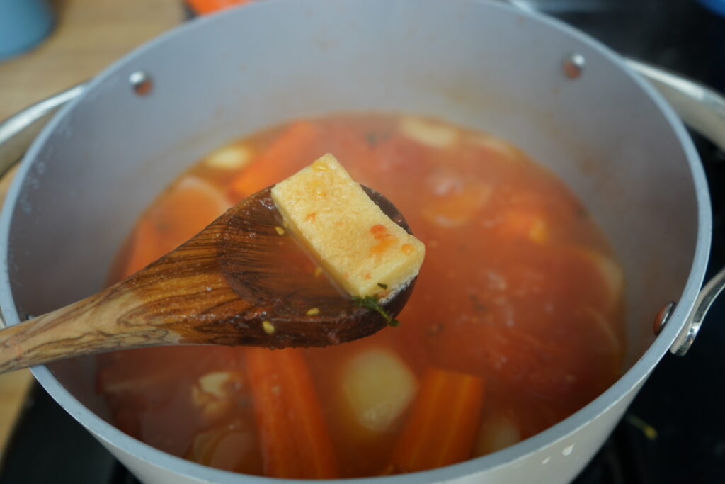 a wooden spoon with a parmesan rind oven a pot of soup