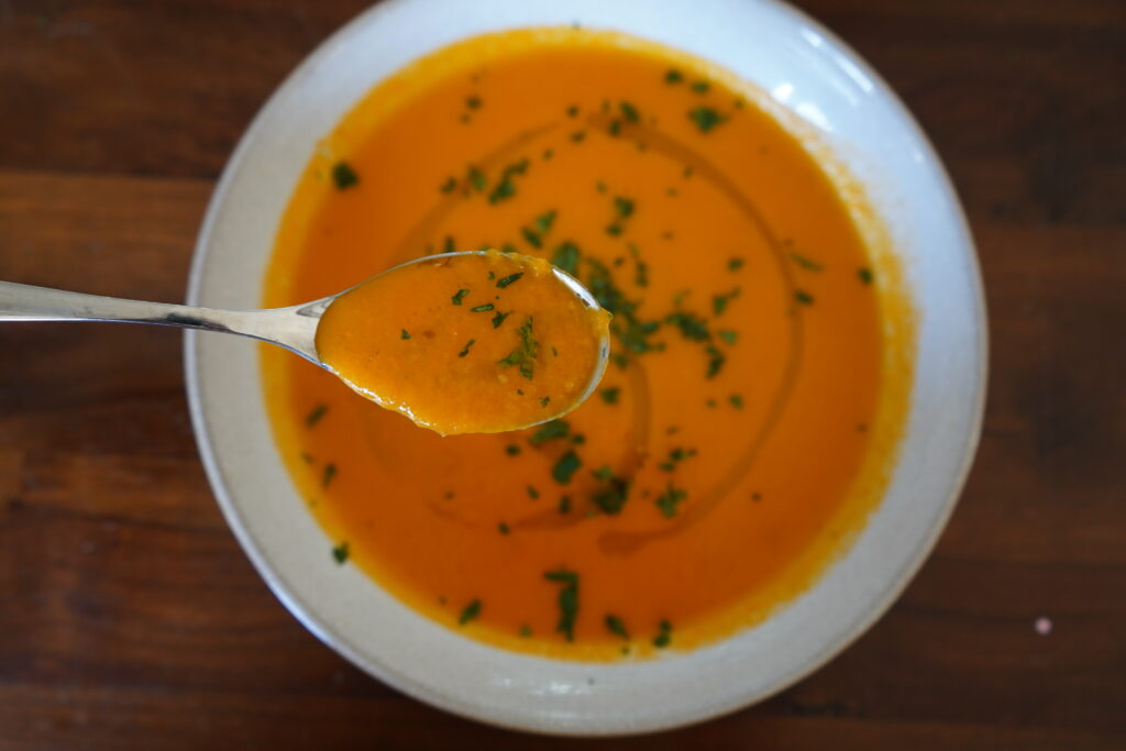 Tomato Soup in a white bowl, being spooned out