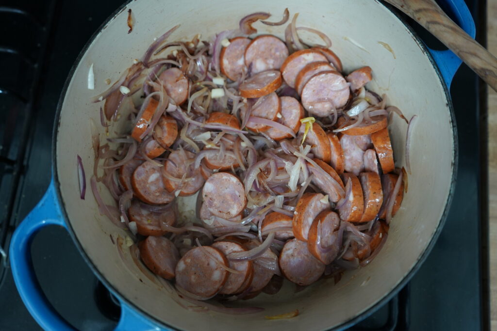 smoked sausages being added to a pot of caramelized onions