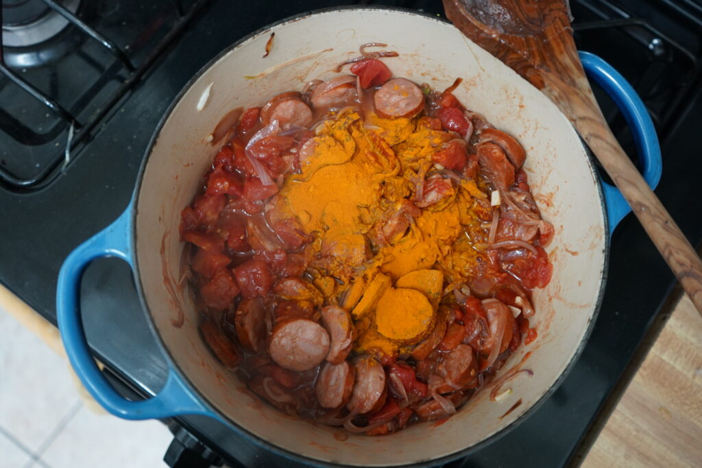 turmeric being add to a pot of smoked sausages and caramelized onions