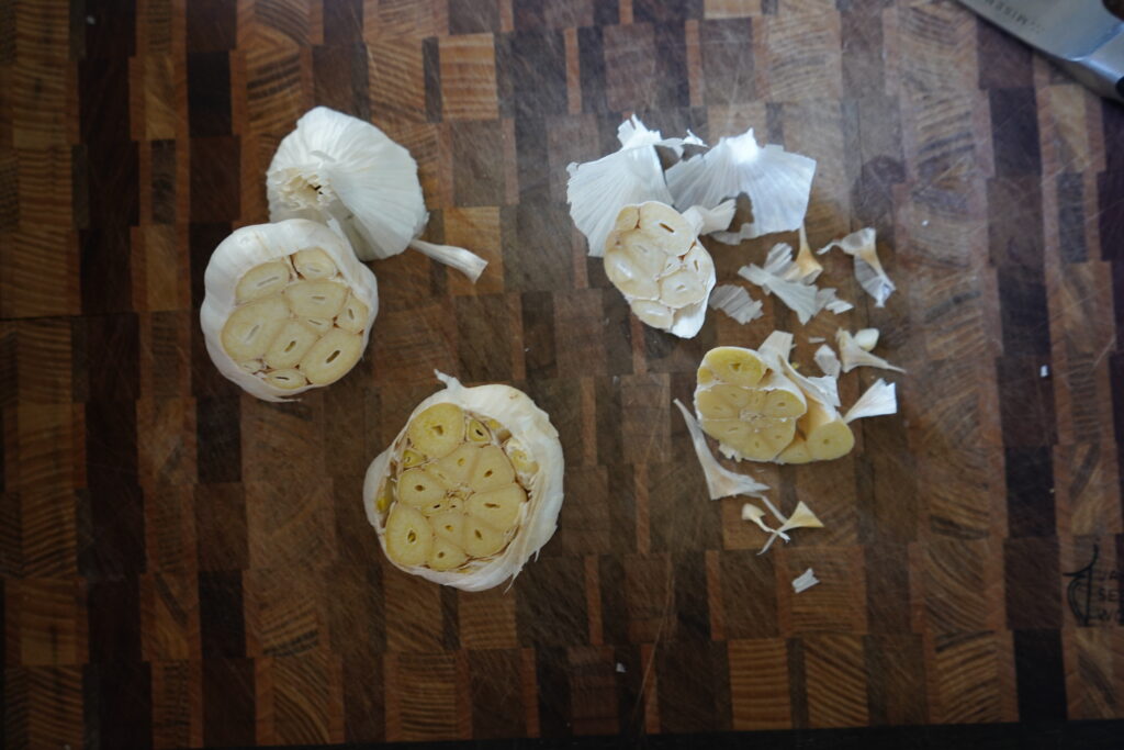 two heads of garlic on a cutting board with the tops cut off