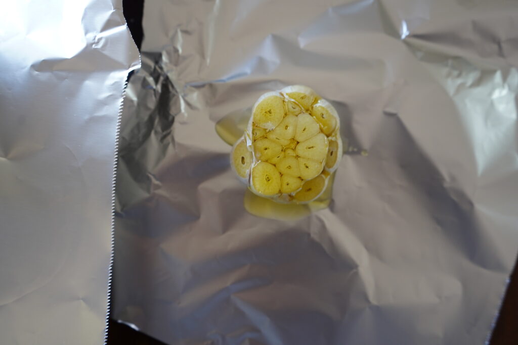 a head of garlic on foil with oil added to it 