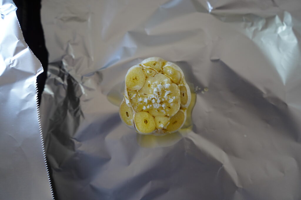 a head of garlic with oil and salt added to it sitting on foil