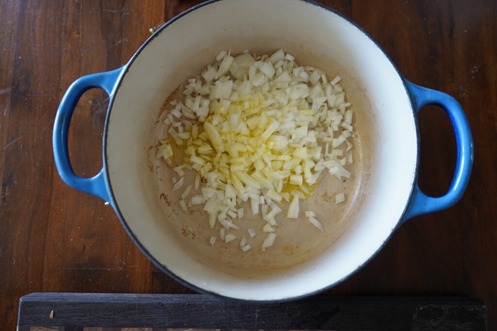 a Dutch oven with chopped onion and olive oil inside