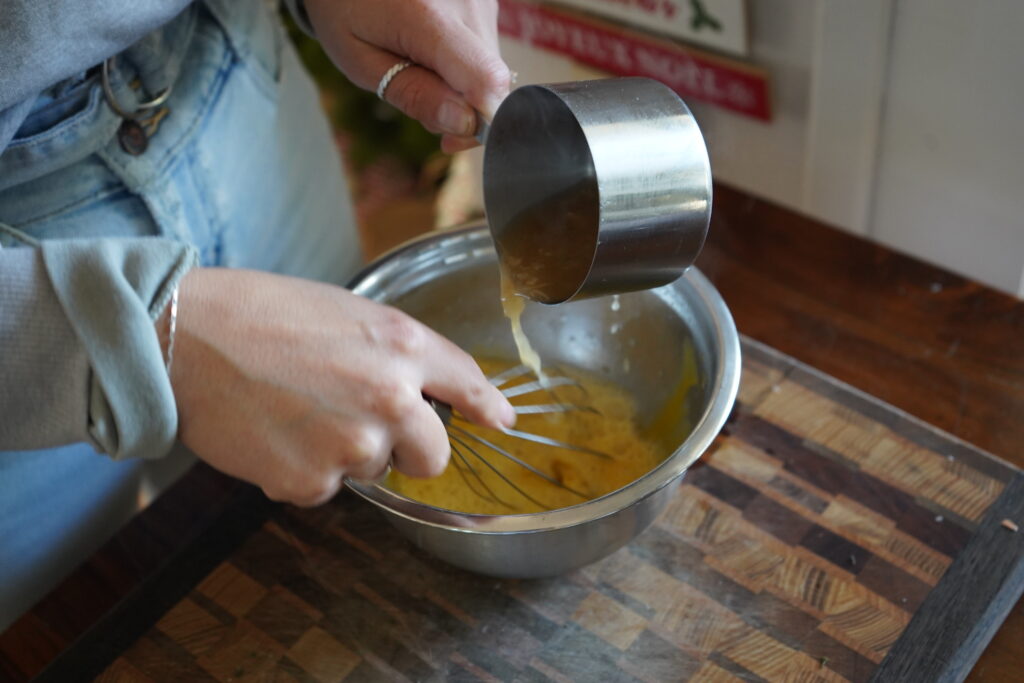 a measuring cup is pouring hot soup over eggs to tempering the eggs 