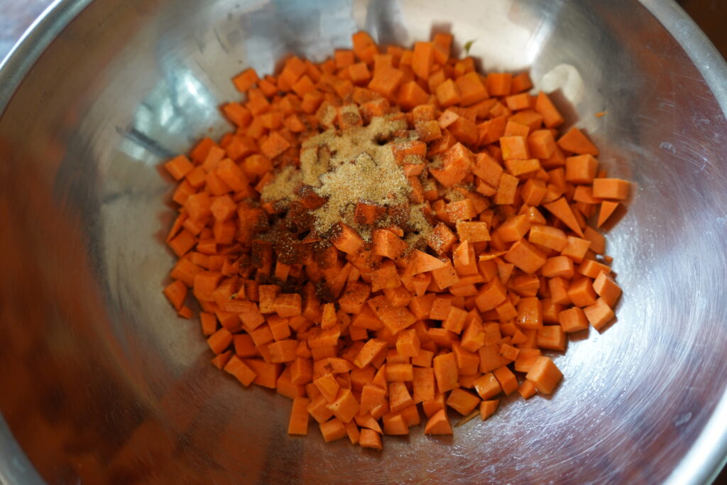 cubed sweet potato in a metal bowl with seasonings on it