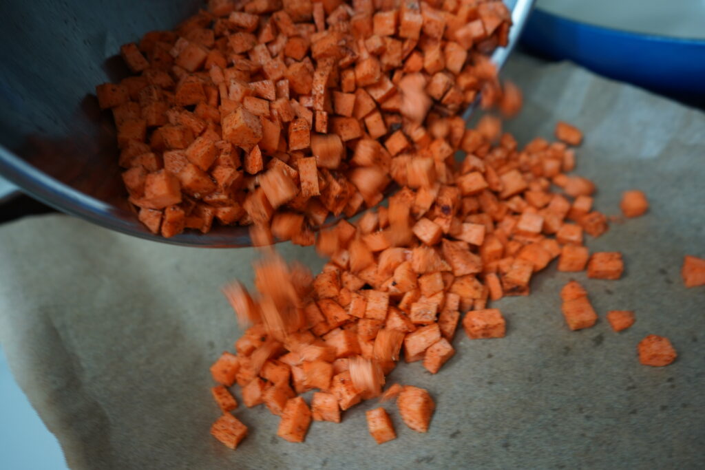 sweet potato that is cubed being poured out of a bowl onto parchment paper