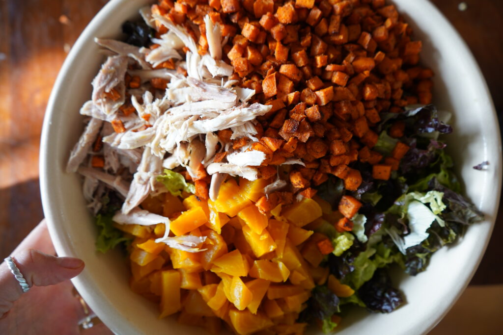 in a salad bowl there is chicken, sweet potato, golden beets and romaine