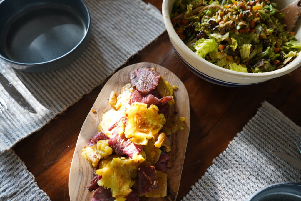 a plate of smashed potatoes next to a big bowl of salad