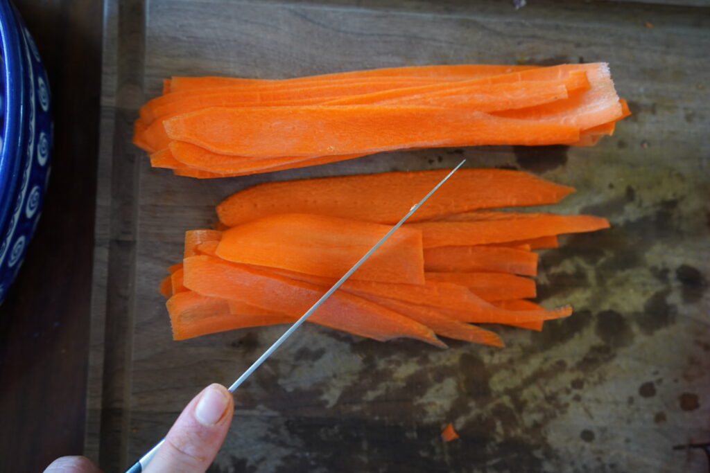 thinly sliced carrots in a pile about to be cut by a knife