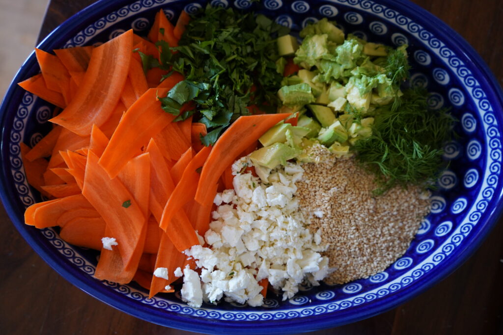 a blue oval salad bowl with carrots, avocado, dill, feta and sesame seeds