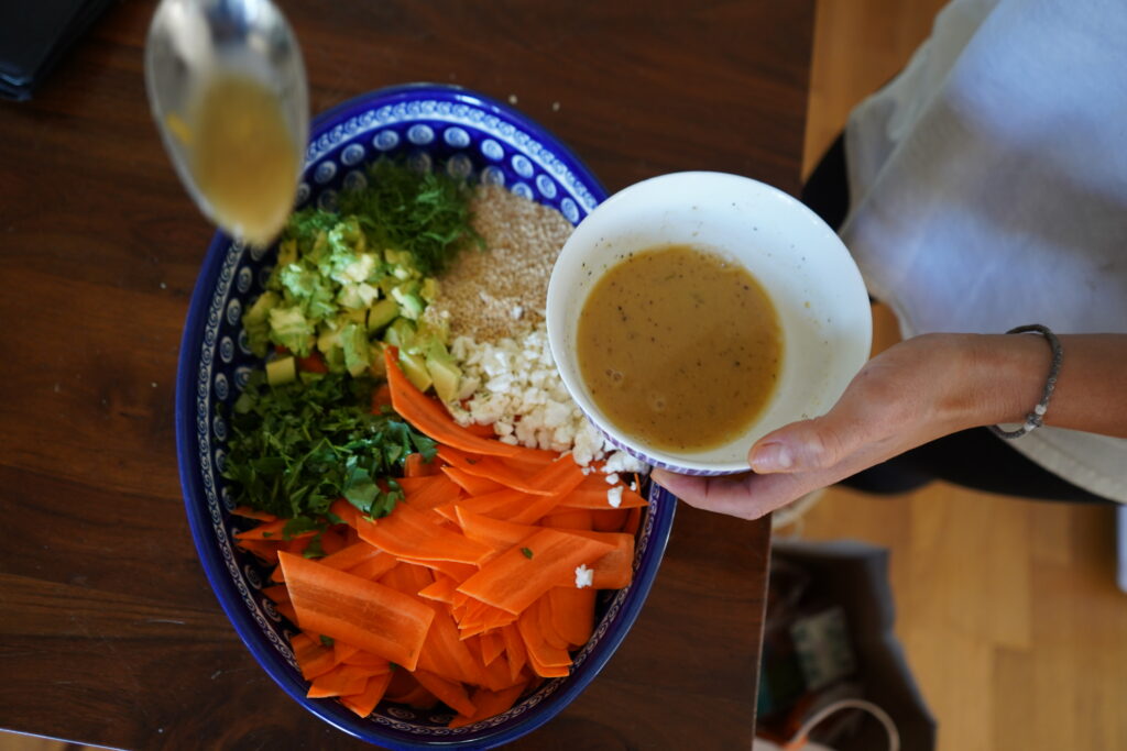 a person holding a bowl of dressing using a spoon to ladel dressing onto a salad