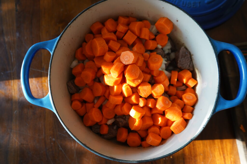 carrots and onions added to a stew pot