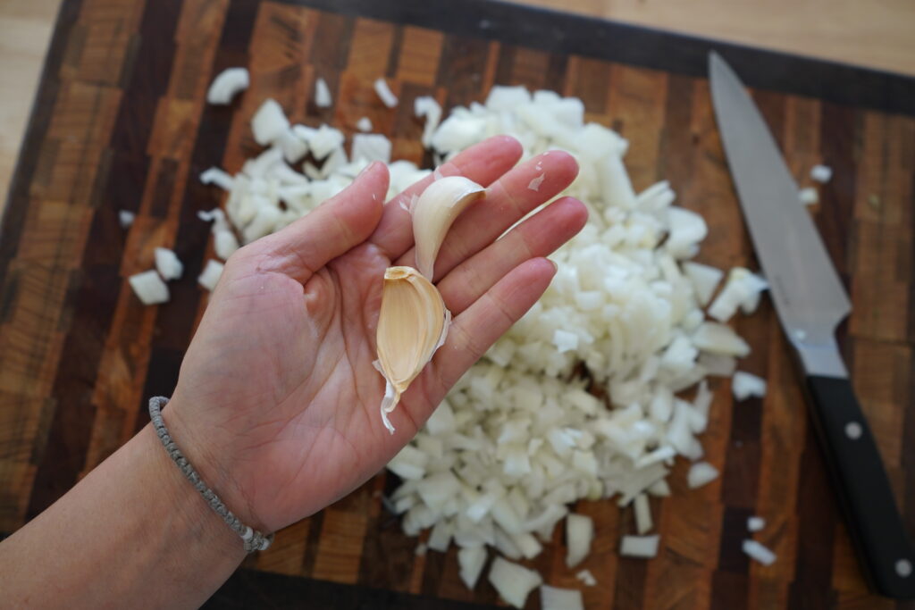 a hand holding garlic over a pile of chopped onion