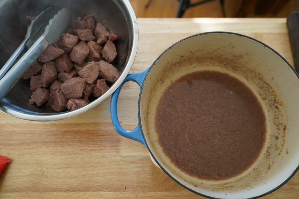 beef chunks in a silver bowl next to a dutch oven