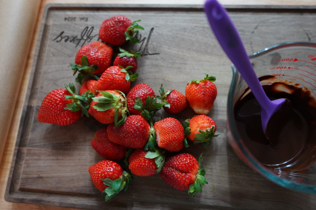 strawberries on a cutting board next to a glass measuring cup of chocolate