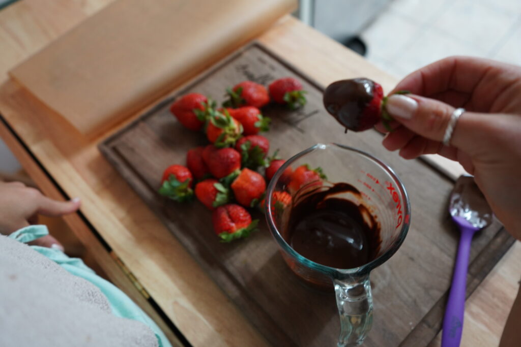 a hand taking a chocolate dipped strawberry out of a bowl of chocolate