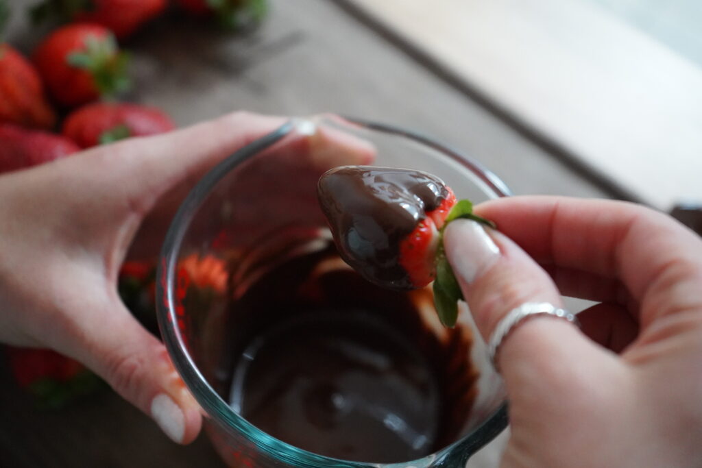 chocolate covered strawberries being dunked in a glass bowl of chocolate