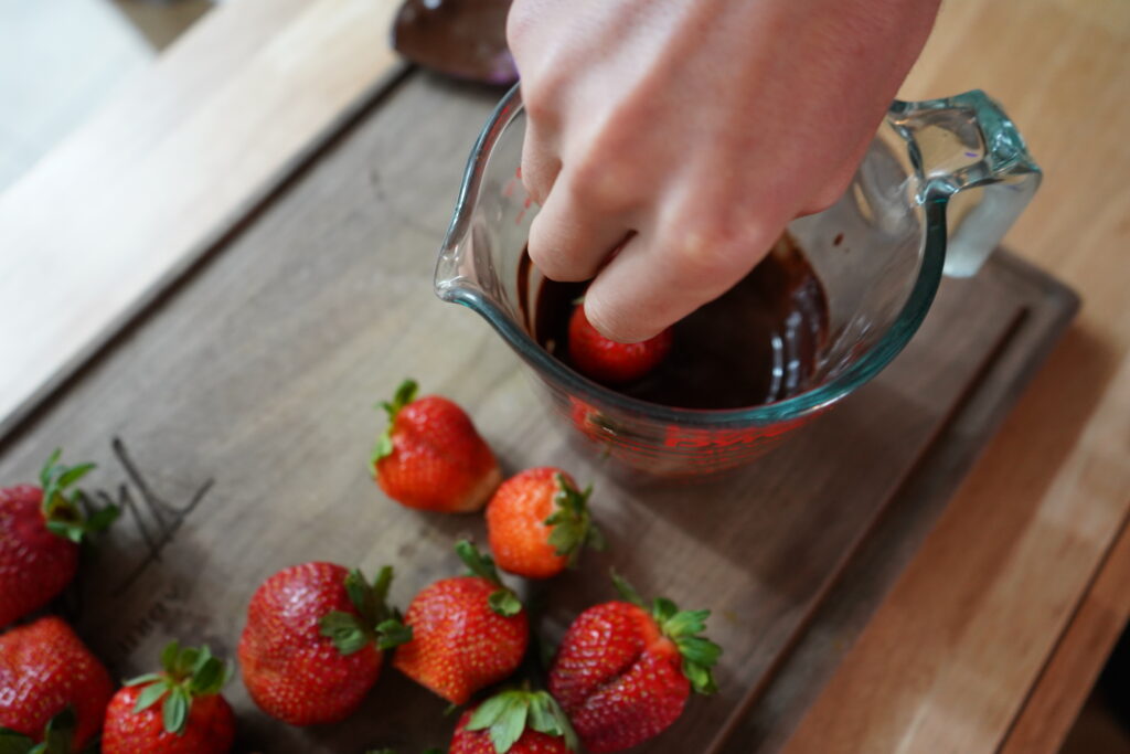 a hand dipping a strawberry in chocolate