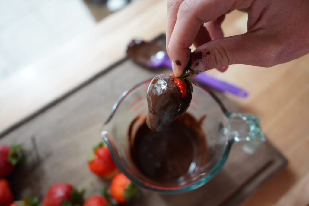 a hand dipping strawberried in chocolate