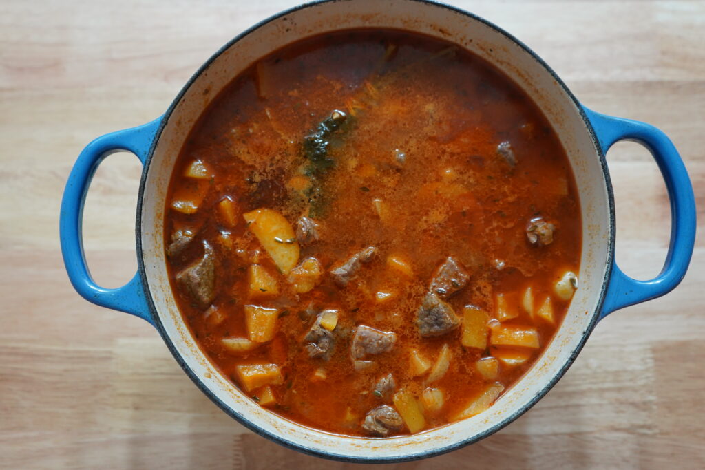 a red looking stew with beef and potatoes peaking through the broth