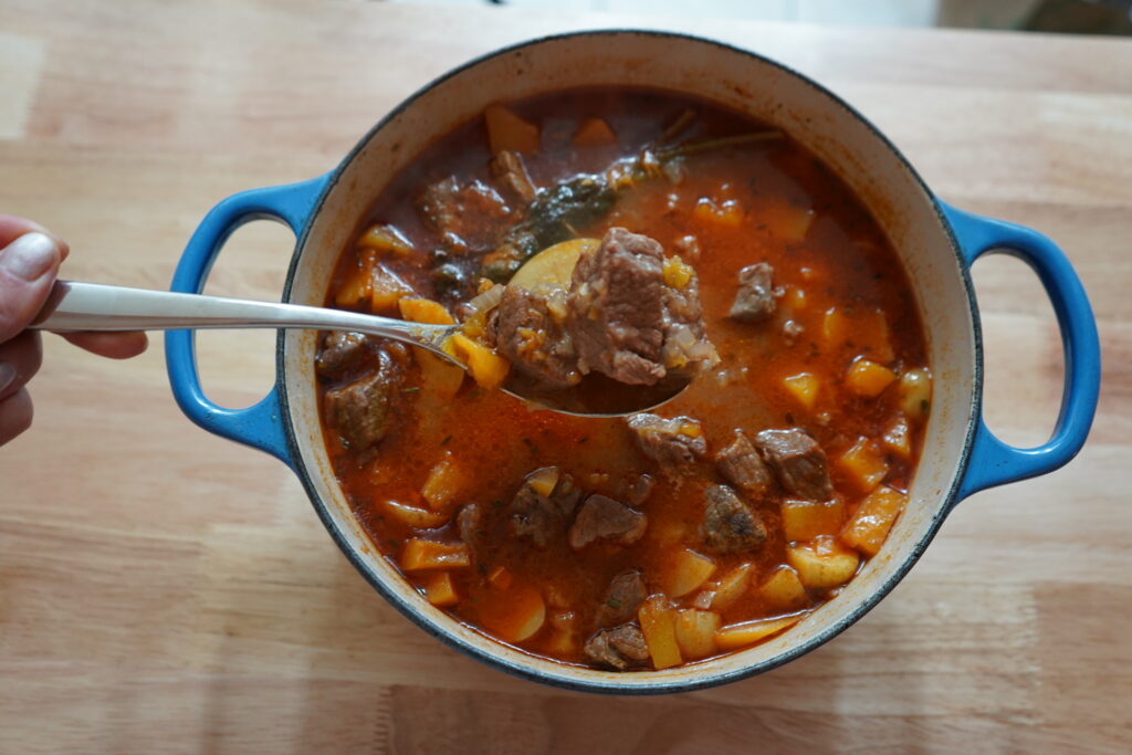 a spoon scooping the beef and potatoes out of the pot.