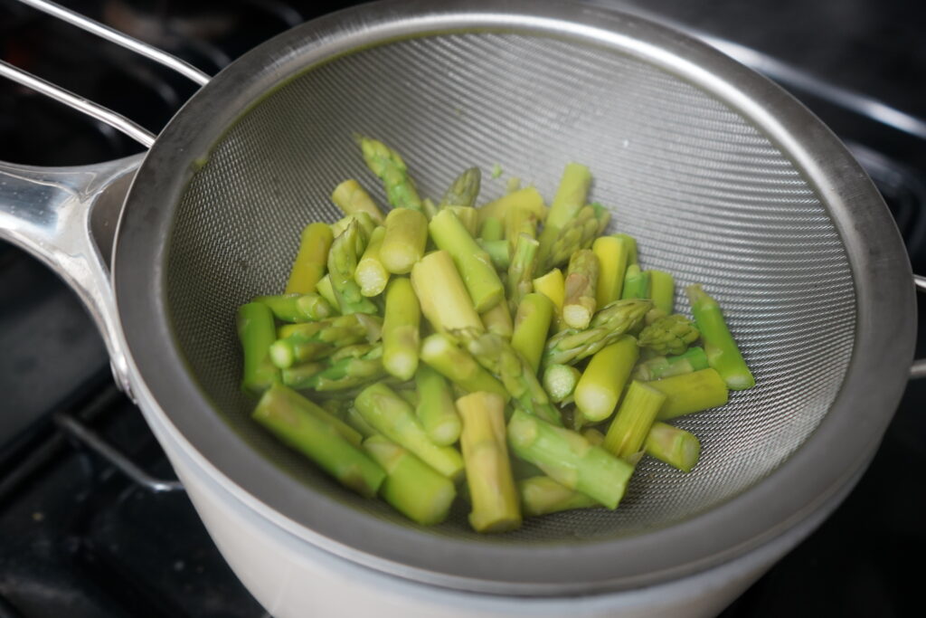 cooked asparagus in a stariner over a pot