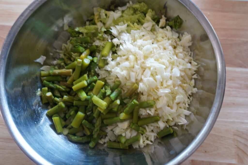 asparagus added to a bowl of lettuces