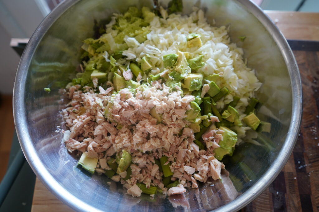 tuna and avocado being added to a salad