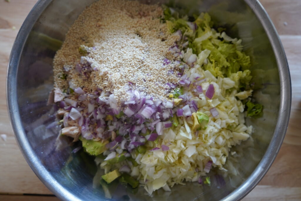 sesame seeds and red onion added to a bowl of lettuce