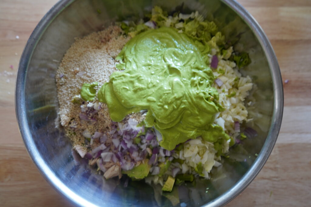 a huge mixing bowl with salad ingredients inside and a blop of green dressing on top