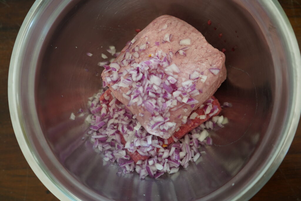 beef, pork and chopped red onion in a mixing bowl