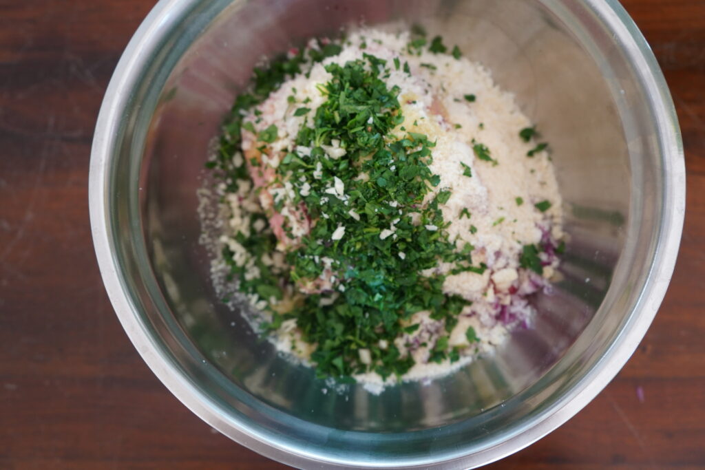 chopped parsley added to a bowl of meat, parmesan, onions and almond flour