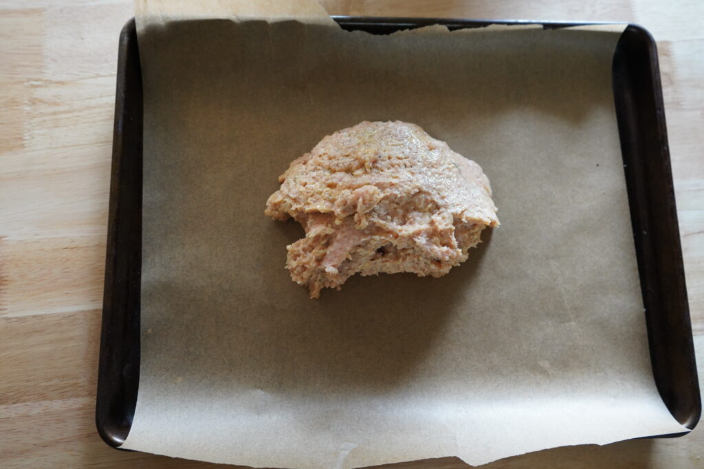 a lump of ground chicken on a pan lined with parchment paper