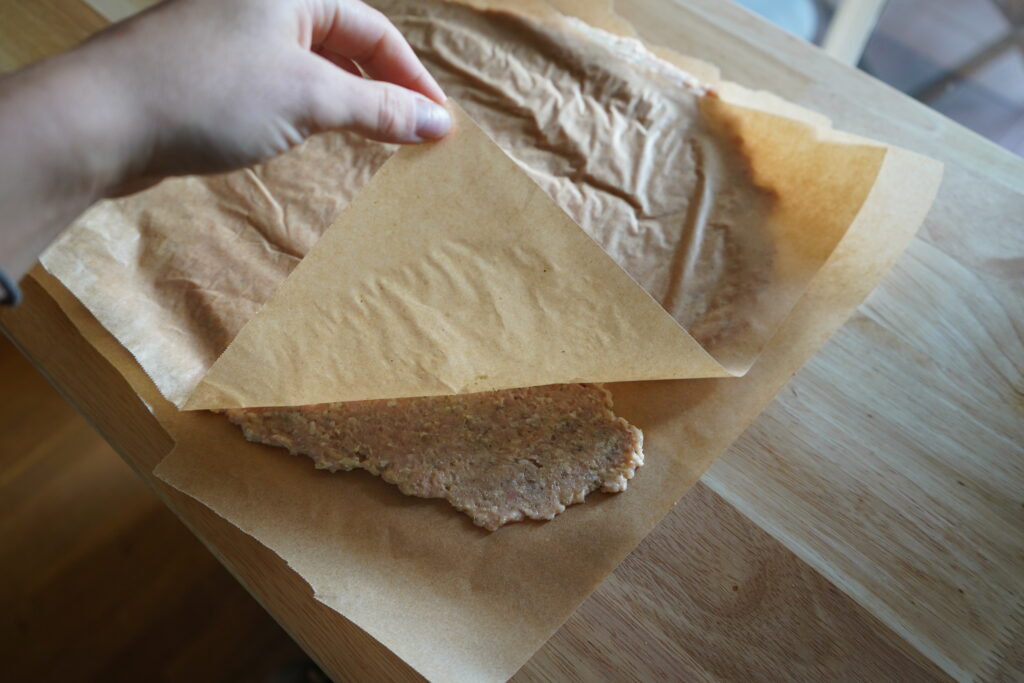 a hand pulling up the above parchment to show the ground chicken