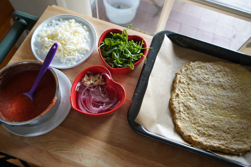 pizza dough on a table waiting to be dressed next to bowls of toppings