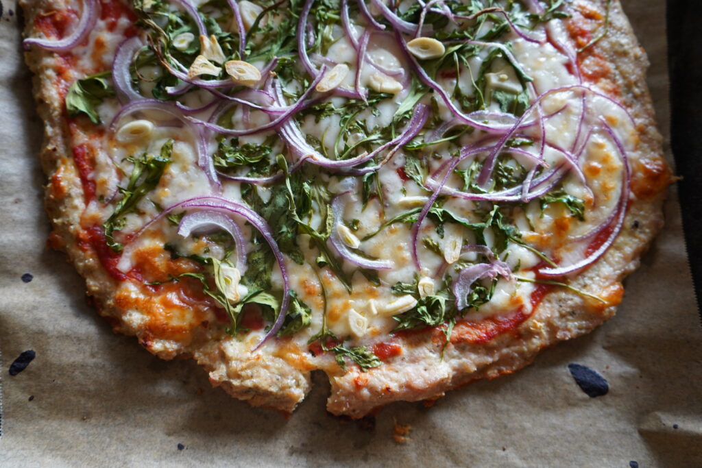 pizza on a parchment paper tray topped with onion and garlic and arugala