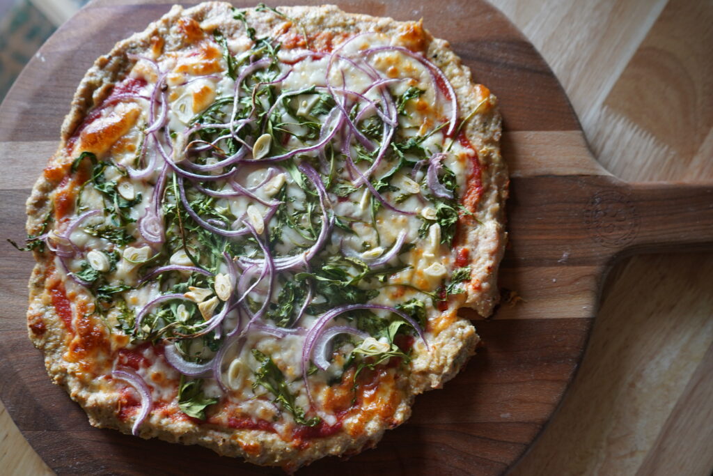 perfectly cooked pizza topped with arugula and onion on a cutting board 