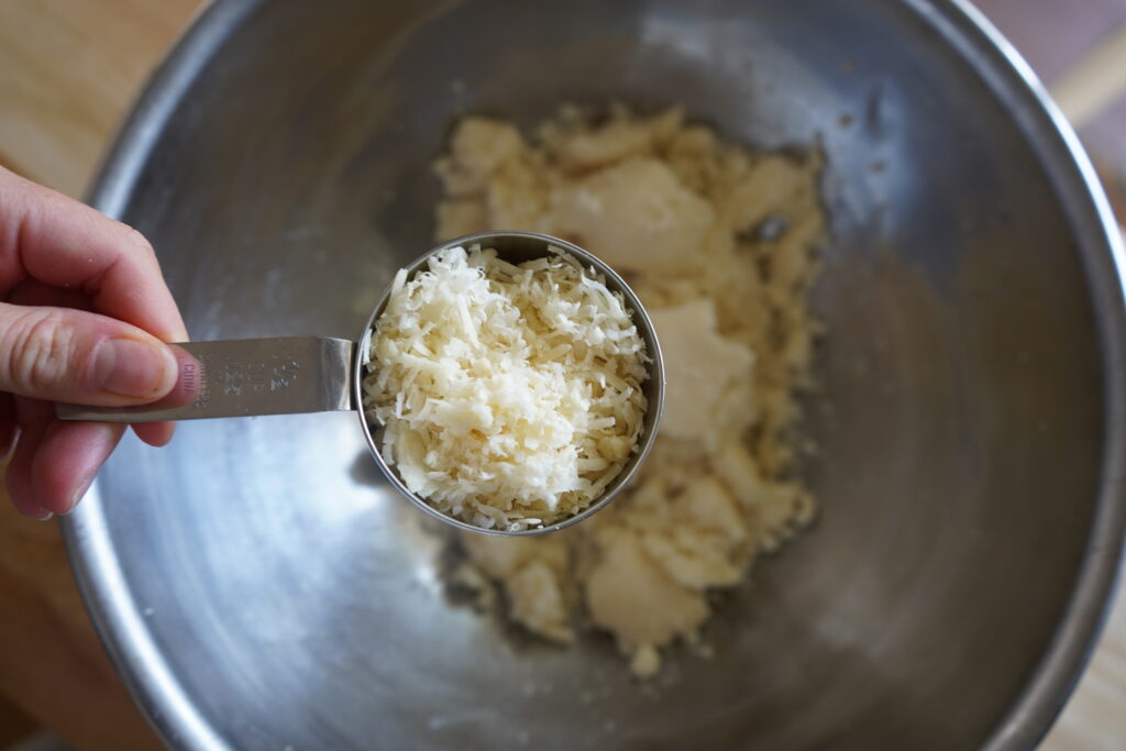 chees ein a measuring cup over a bowl of minced cauliflower