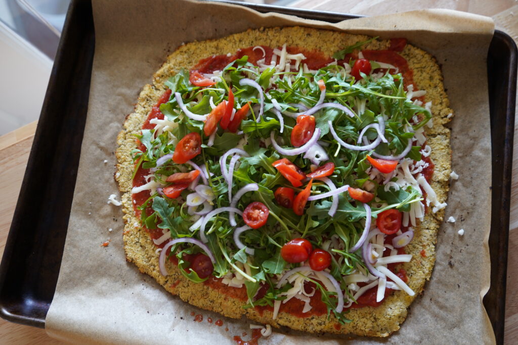 cauliflower crusted pizza topped with arugula and tomatoes